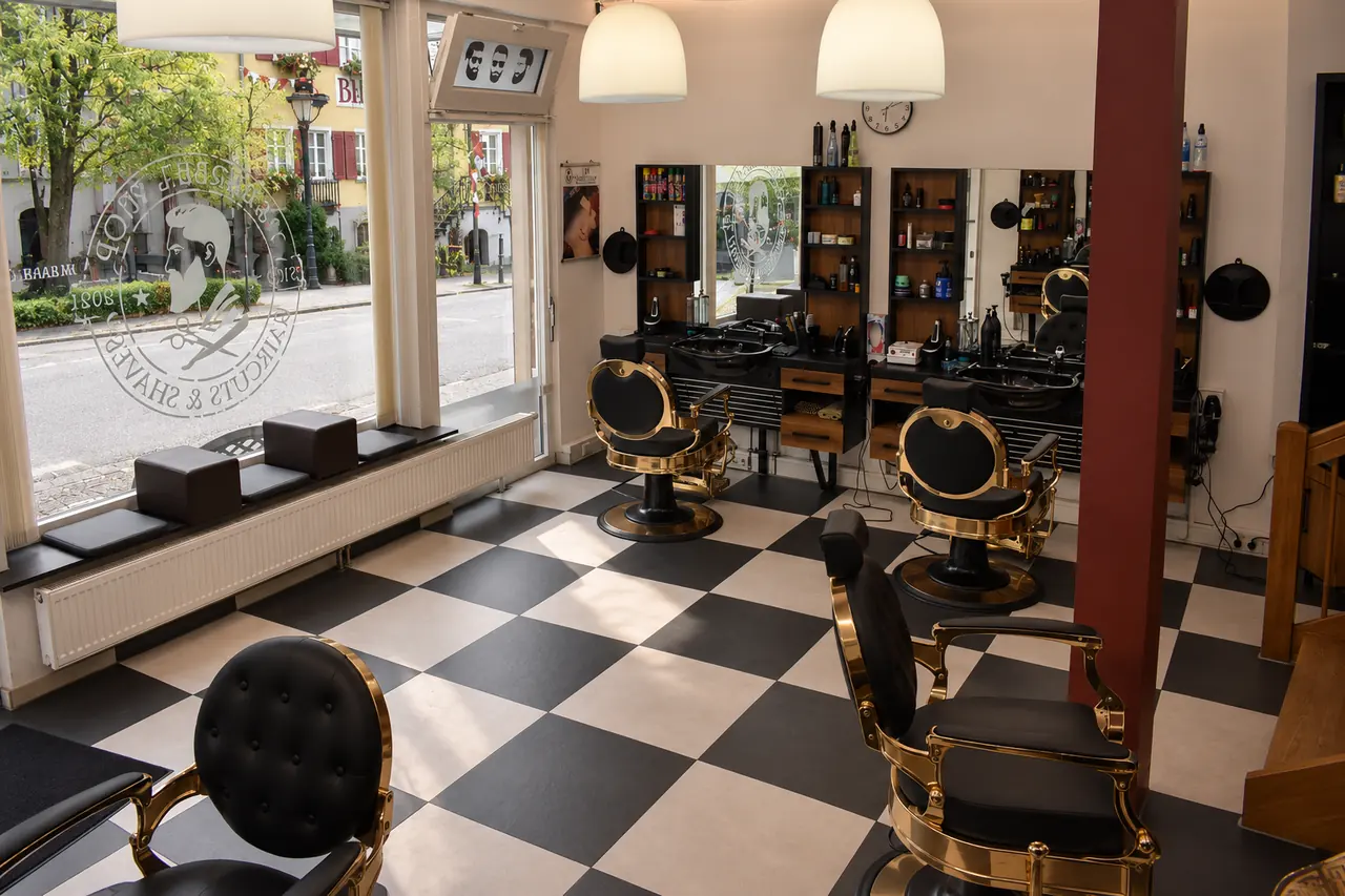 JM Barber von innen: schwarz-weißer Schachbrettboden, Barber-Stühle mit goldenen Details