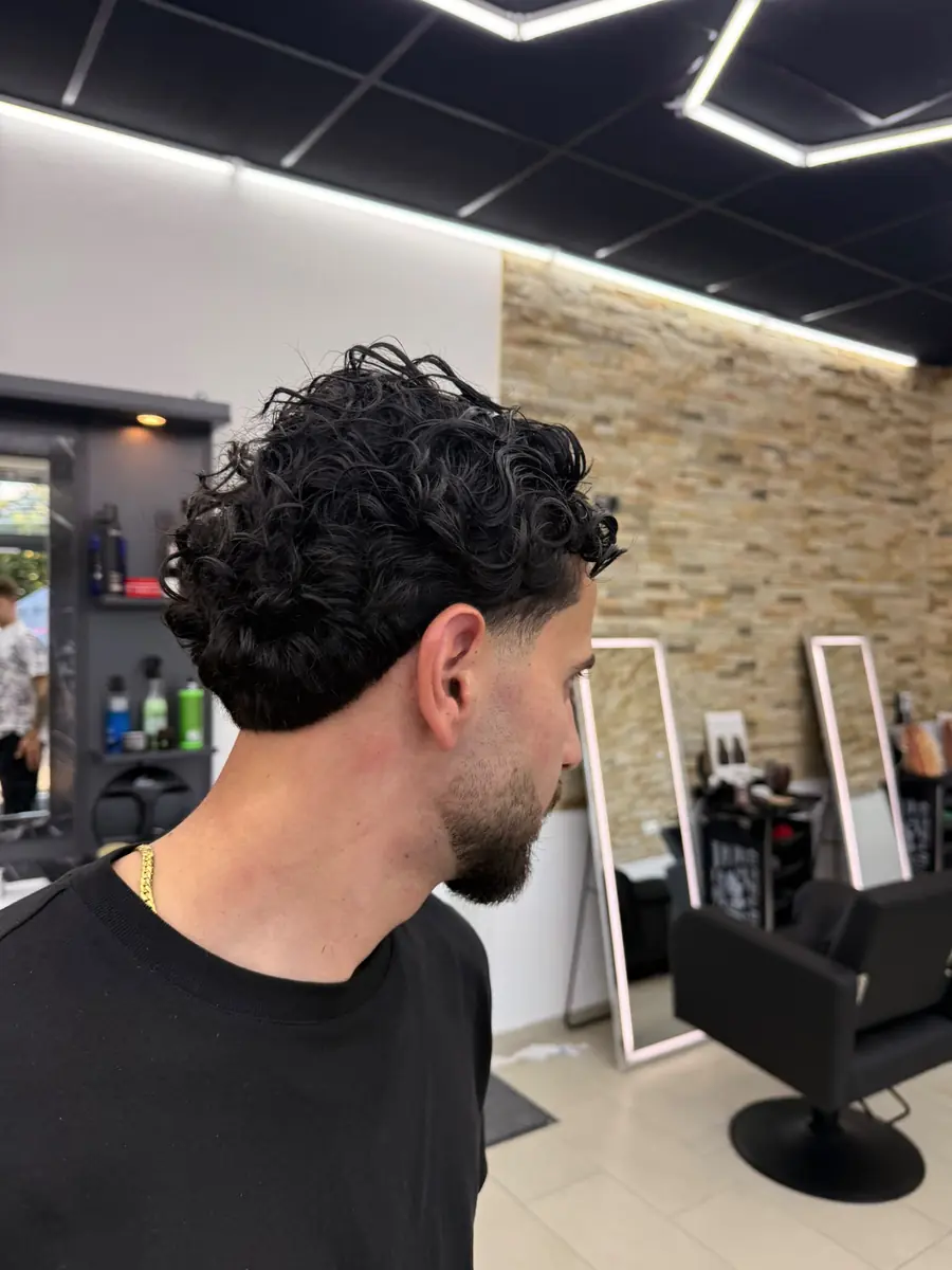 Frischer Haarschnitt mit Fade und Locken von der Seite, im Hintergrund der Salon