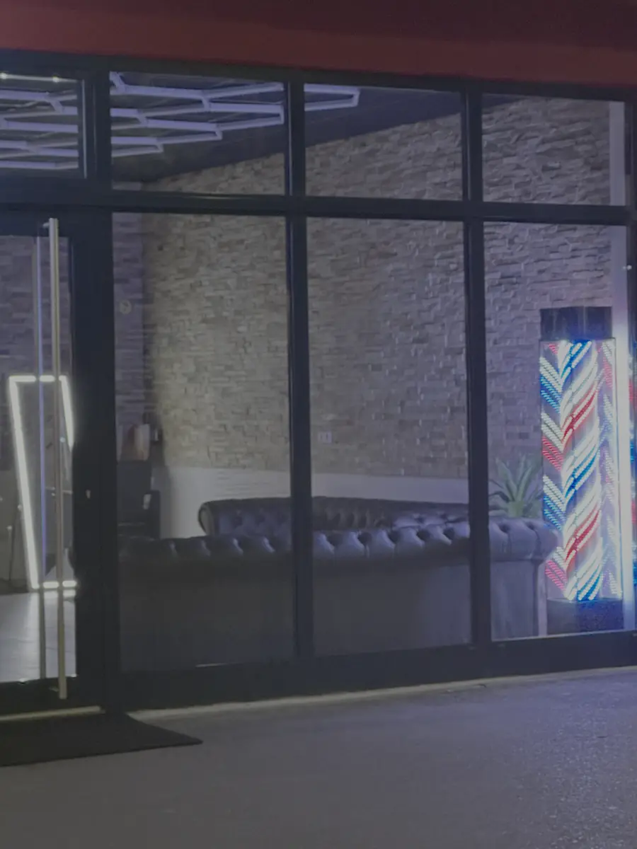 JM Barbershop am Abend: beleuchteter Barber-Pole und Lounge hinter der Glasfront